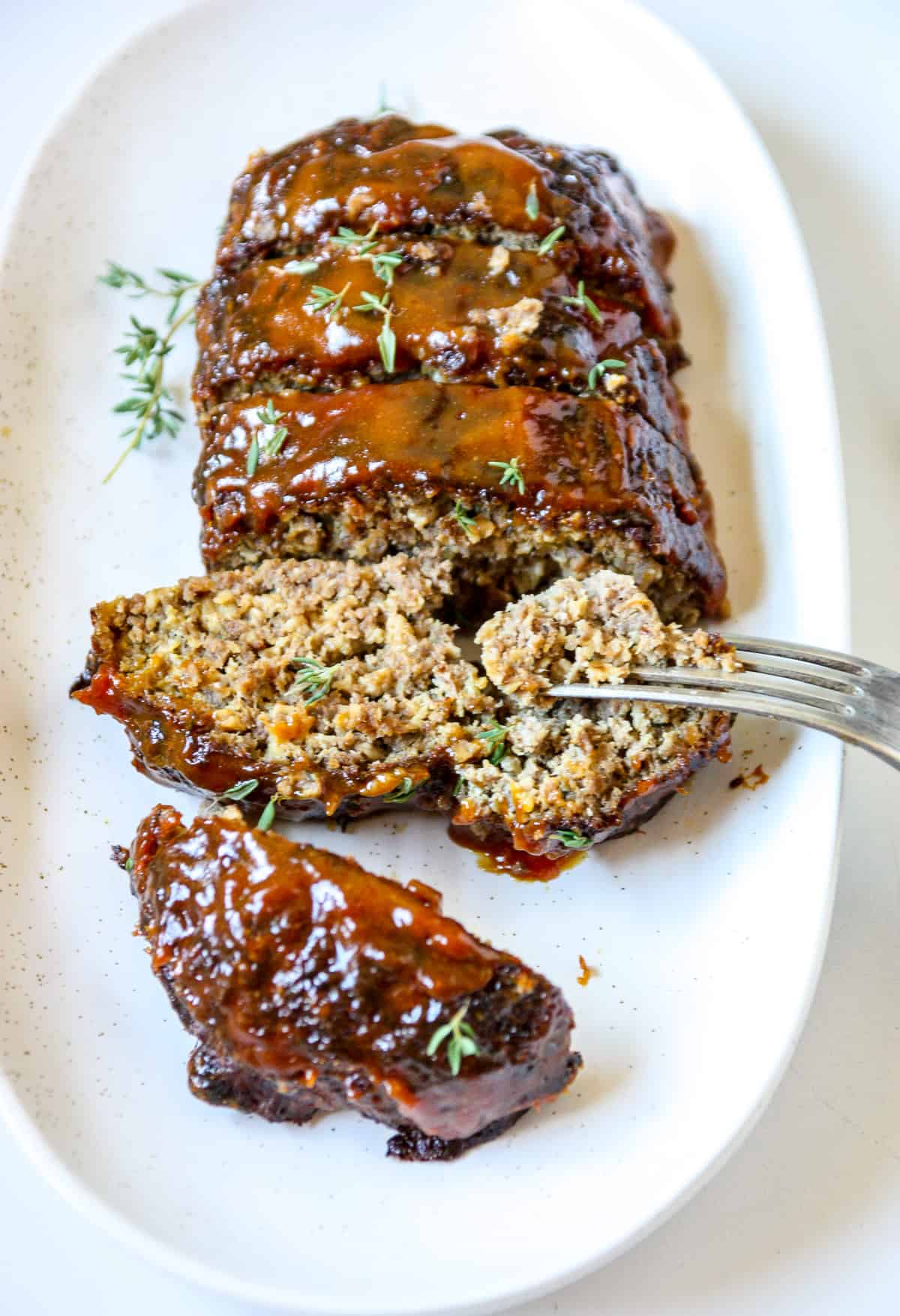 A silver fork cutting into a slice of meatloaf on a white plate.