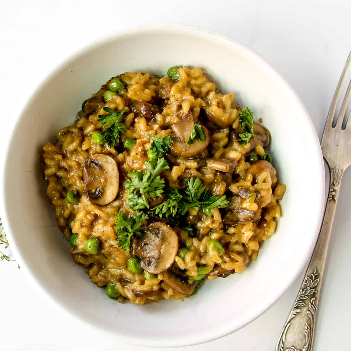 Mushroom pea risotto in a white bowl, garnished with parsley.