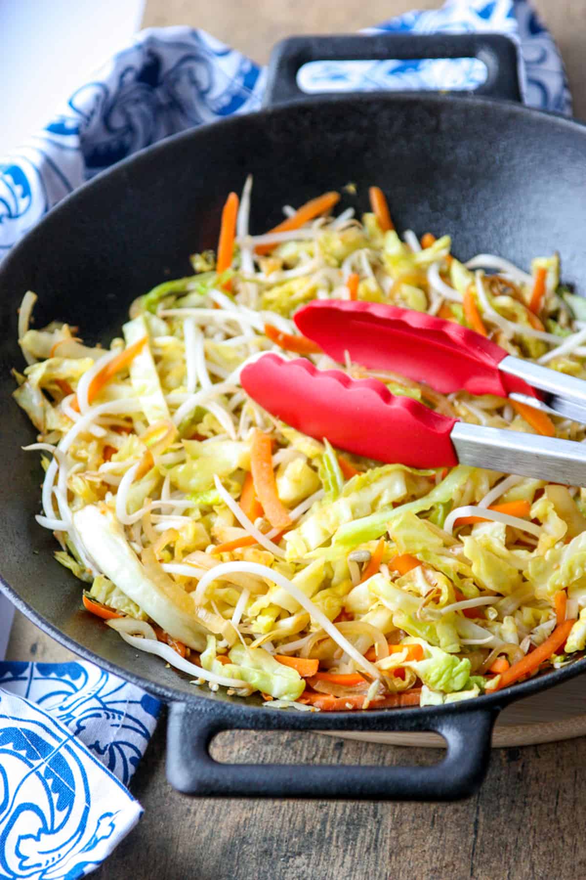 Finished cabbage stir fry in a cast iron wok with tongs for serving.