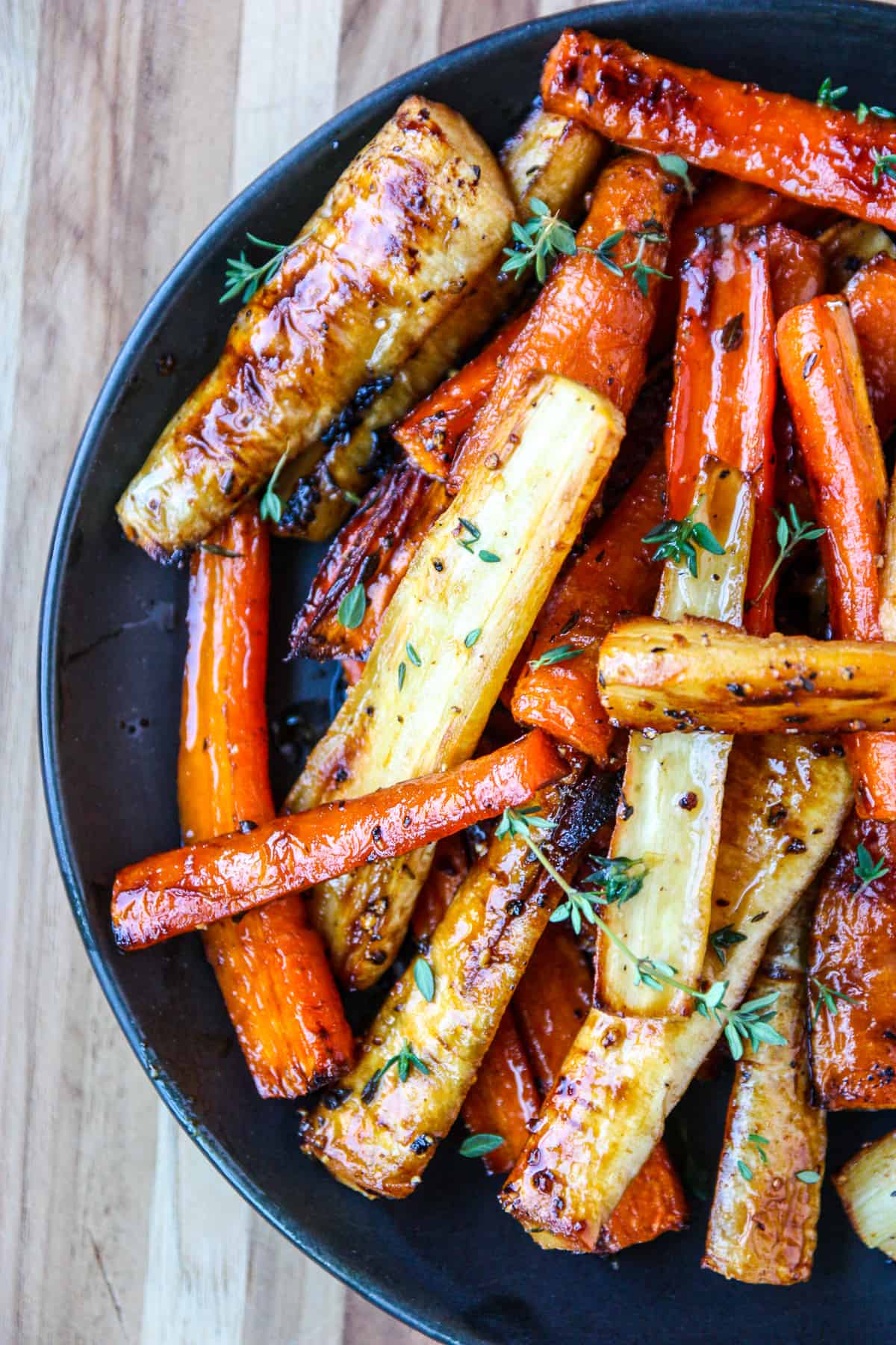 Honey roasted carrots and parsnips on a black plate garnished with thyme.