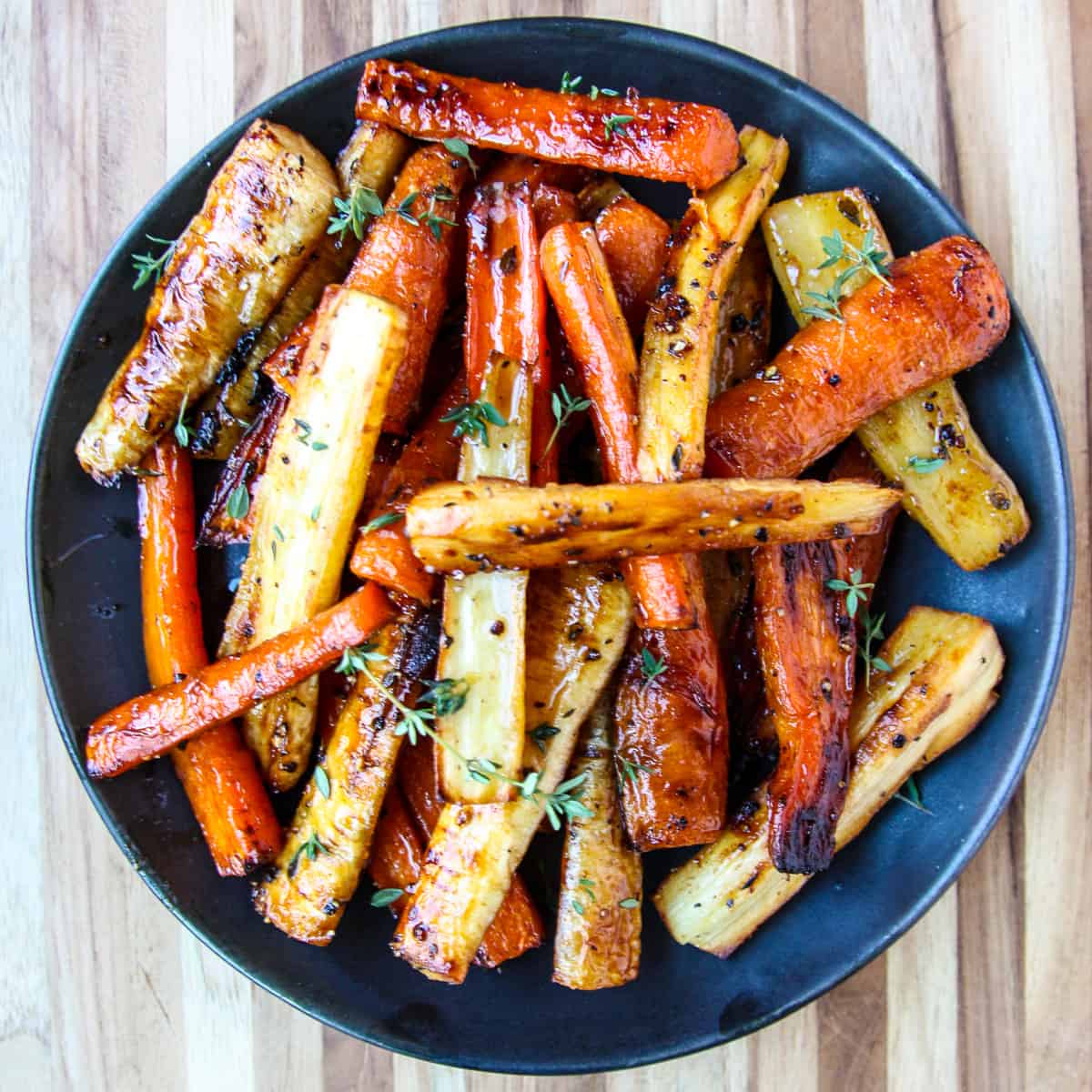 Roasted carrots and parsnips on a black plate.