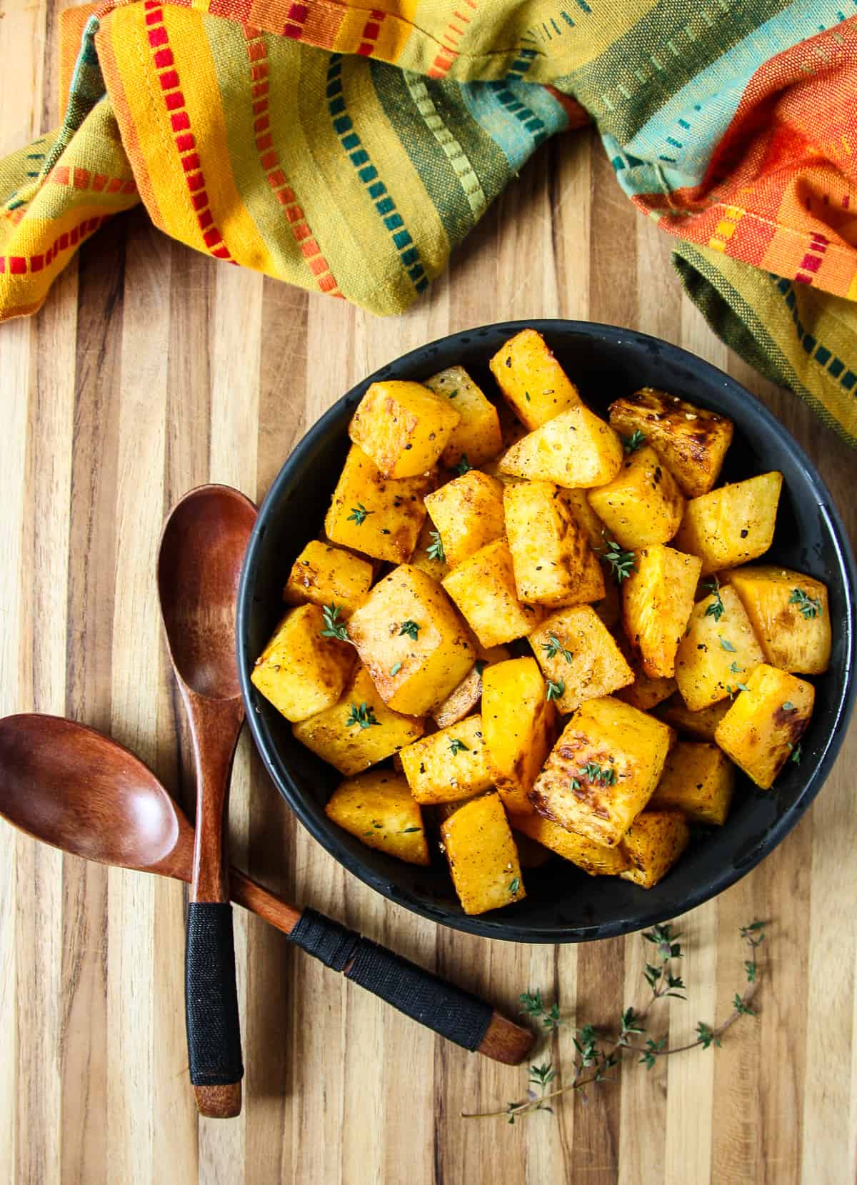 Roasted rutabaga cubes in a black bowl  and two wooden spoons on a wooden board.