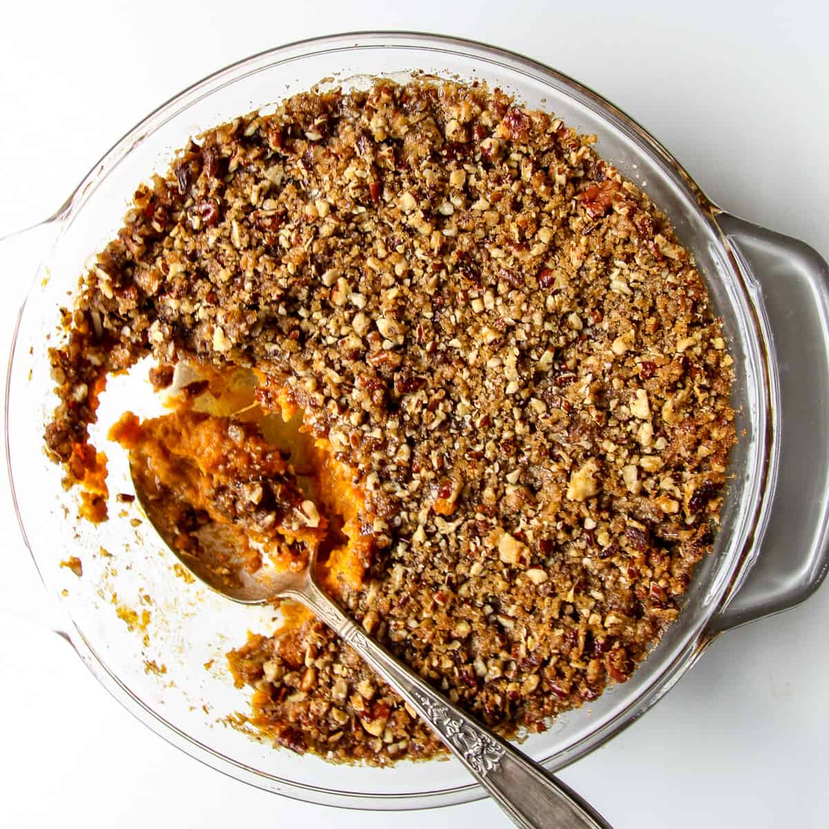 A serving spoonful of sweet potato crunch being taken from a casserole dish.