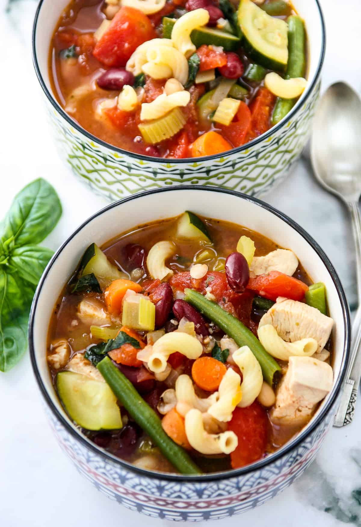 Two bowls of chicken minestrone soup and two silver spoons.