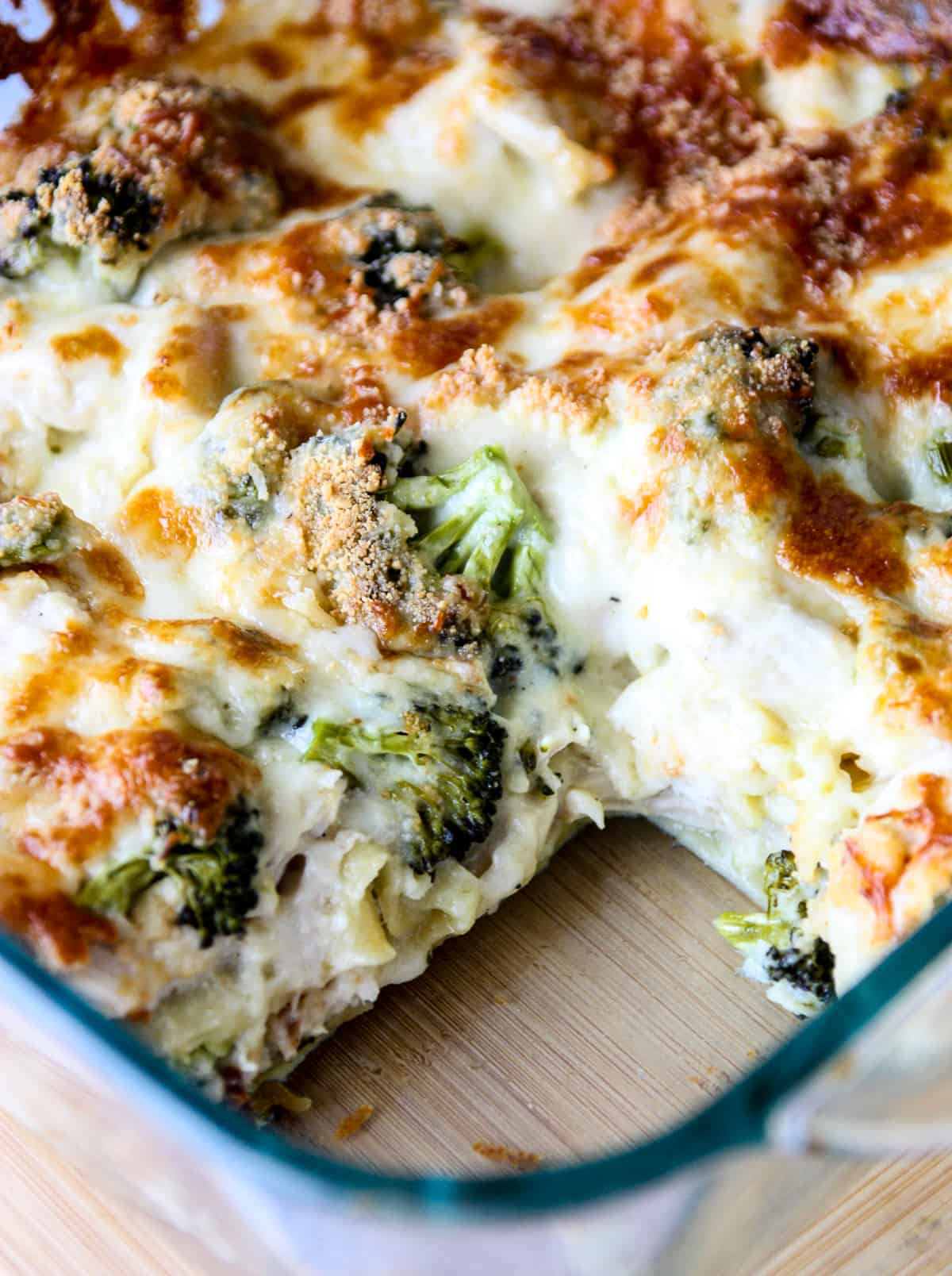 Broccoli and cheese lasagna alfredo in a glass baking dish with one slice removed.