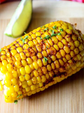 A piece of Cajun corn on the cob on a wooden board with corn shaped corn holders in either end.