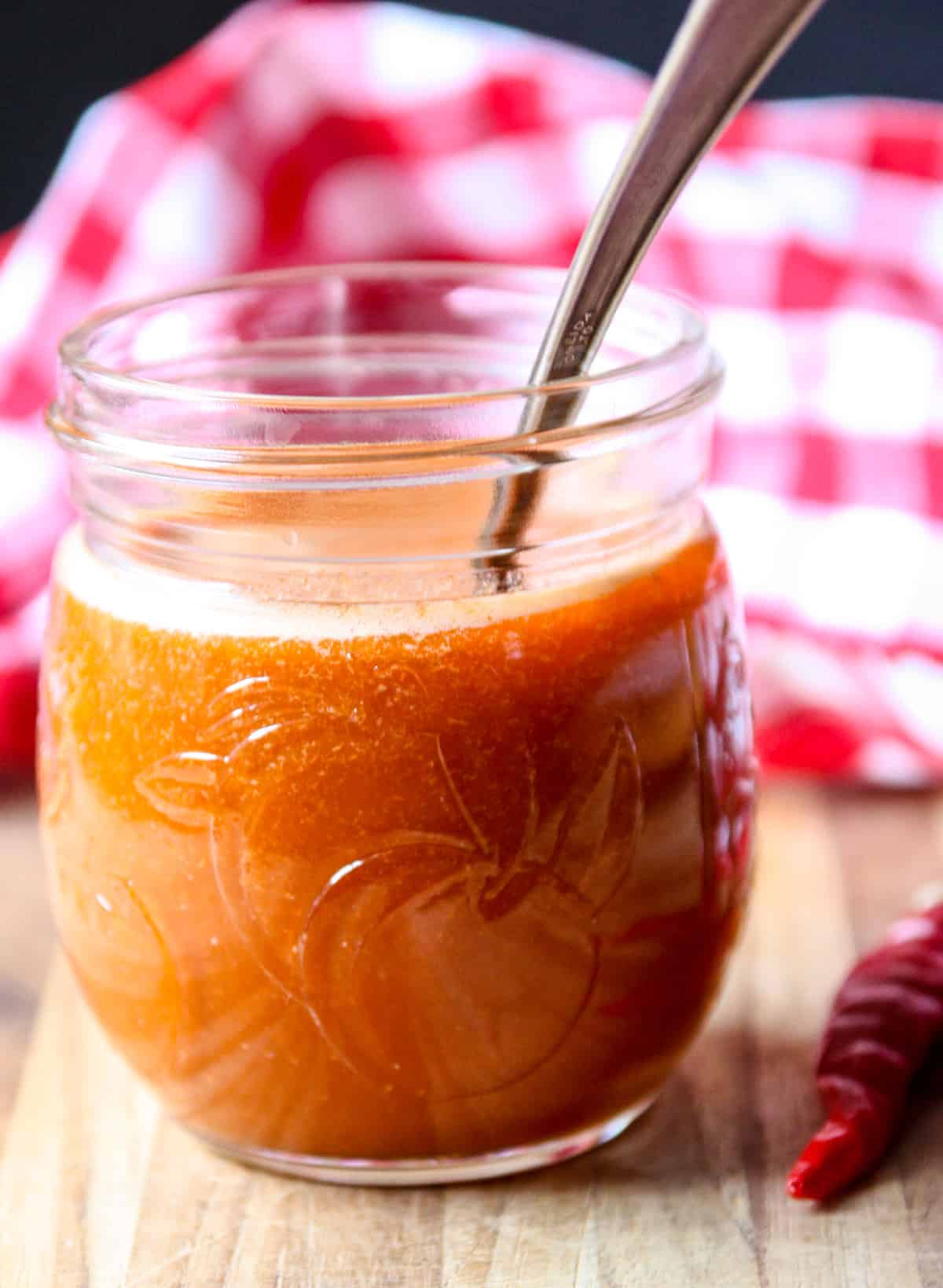 Cayenne pepper sauce in a glass jar next to a cayenne chili pepper.