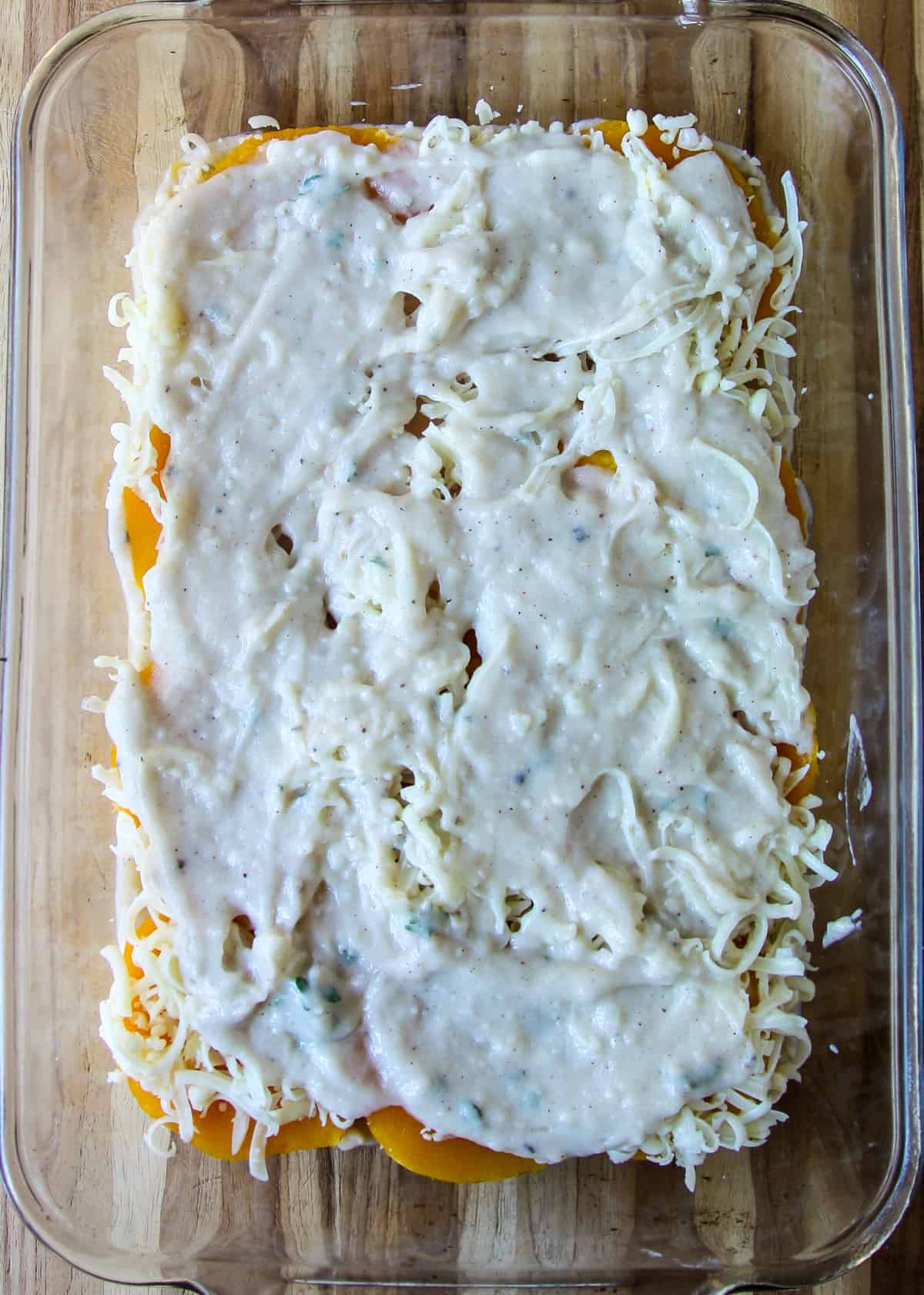 Bechamel sauce spread over squash and cheese in lasagna dish.