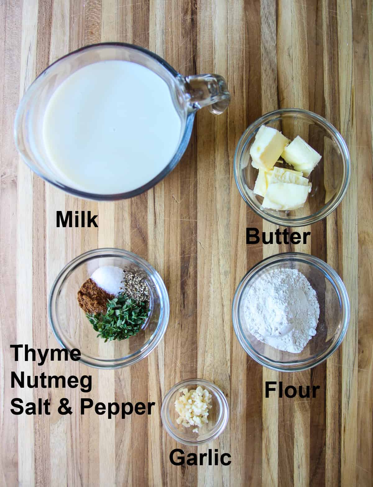 The ingredients for the béchamel sauce in glass dished on a wooden board.