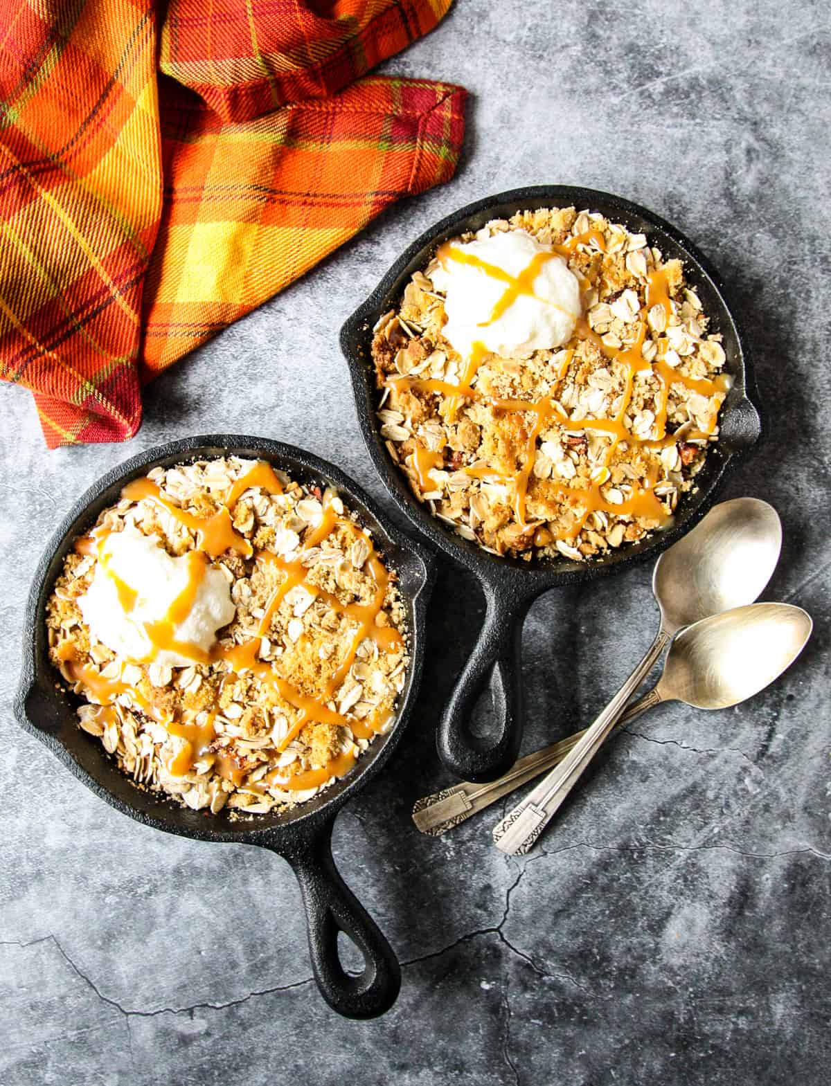 Air fryer apple crisp in two mini cast iron skillets on a dark grey counter top.