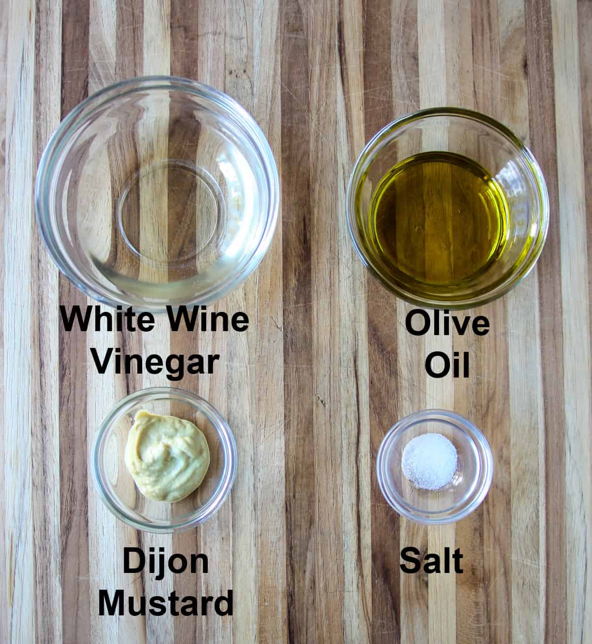 The ingredients for the salad dressing in glass bowls, on a wooden board.