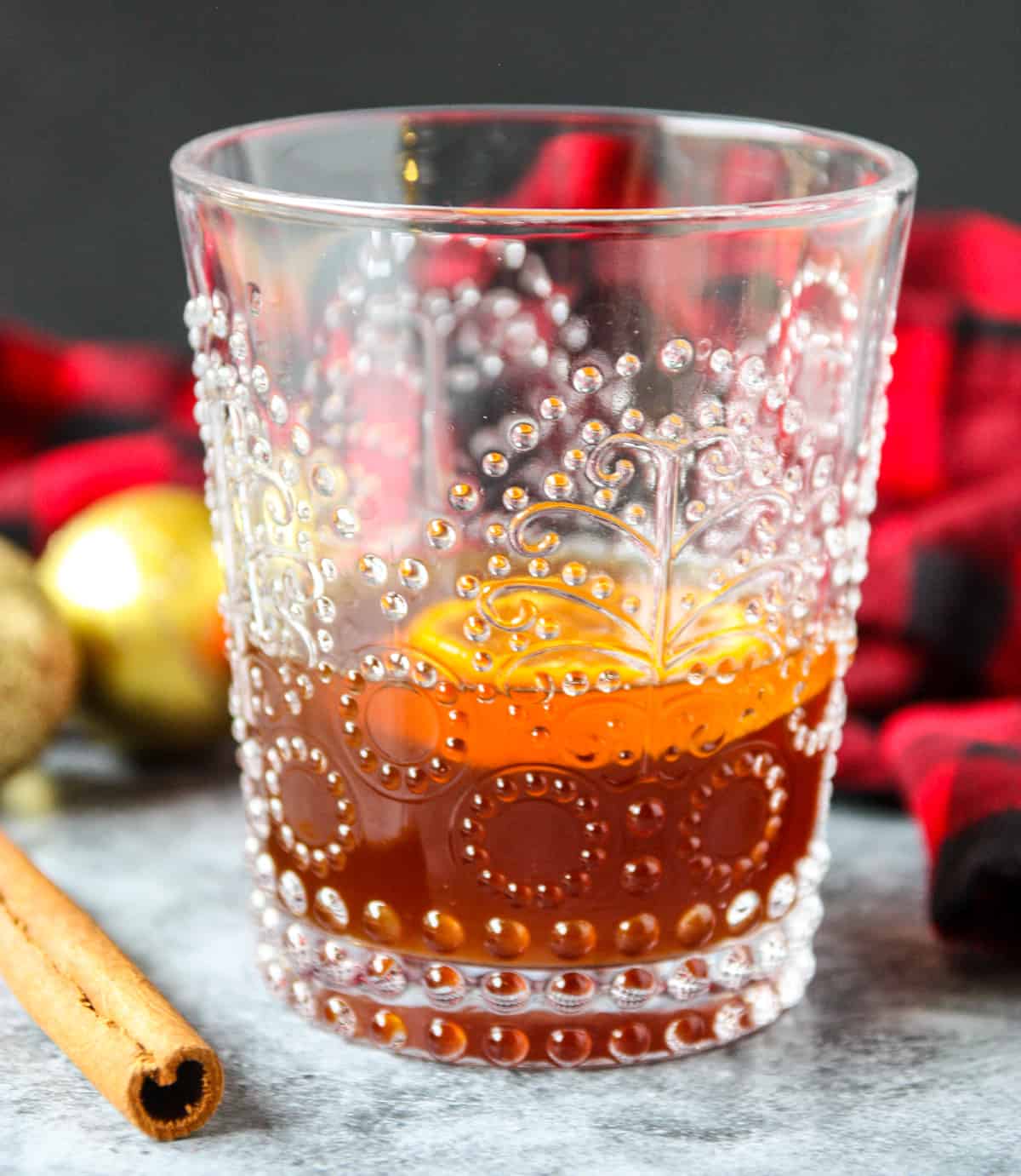 A gingerbread old fashioned cocktail in a glass, with Christmas balls in the background.