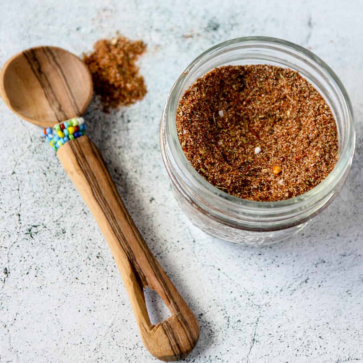 Chicken taco seasoning in a glass jar with a small wooden spoon.