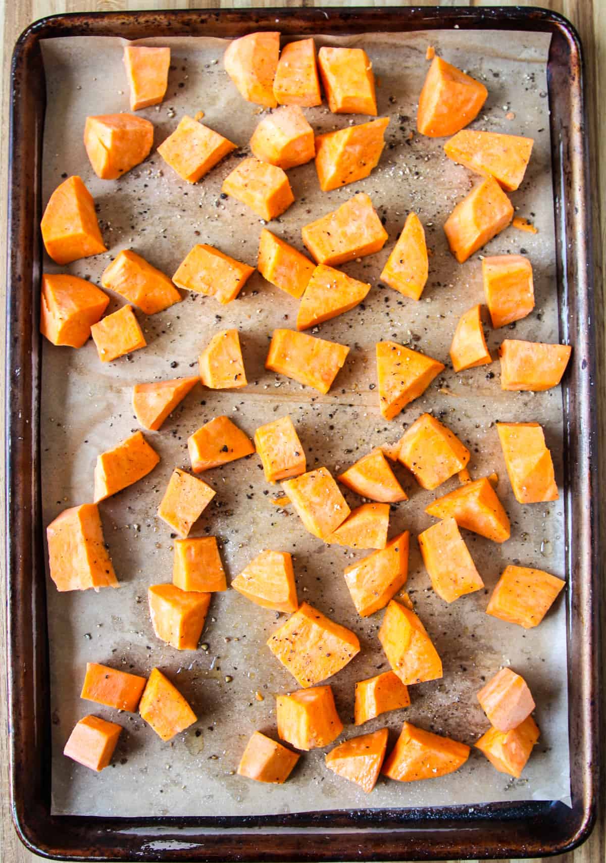 Cubes of raw sweet potato on a parchment lined baking sheet.