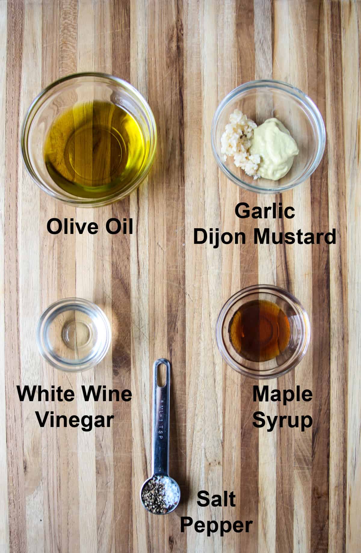 The ingredients for the salad dressing, in glass bowls on a wooden board.