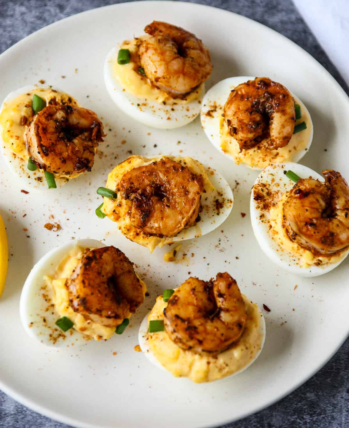 Cajun shrimp deviled eggs on a white plate with lemon wedges.