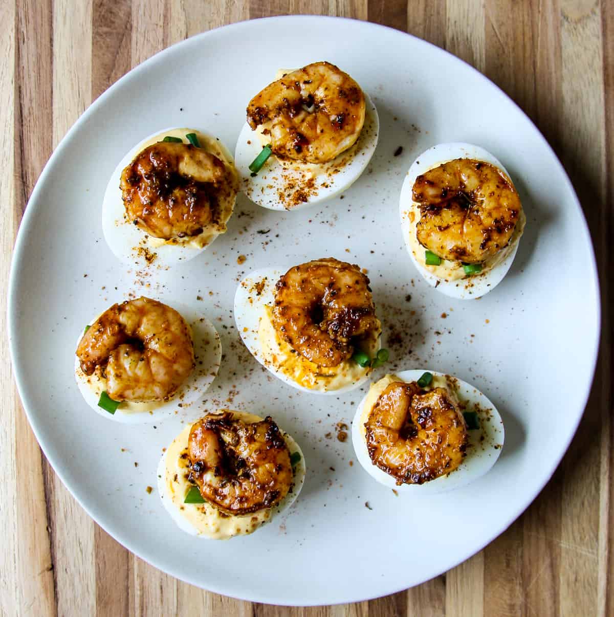 Deviled eggs topped with Cajun shrimp on a white plate.