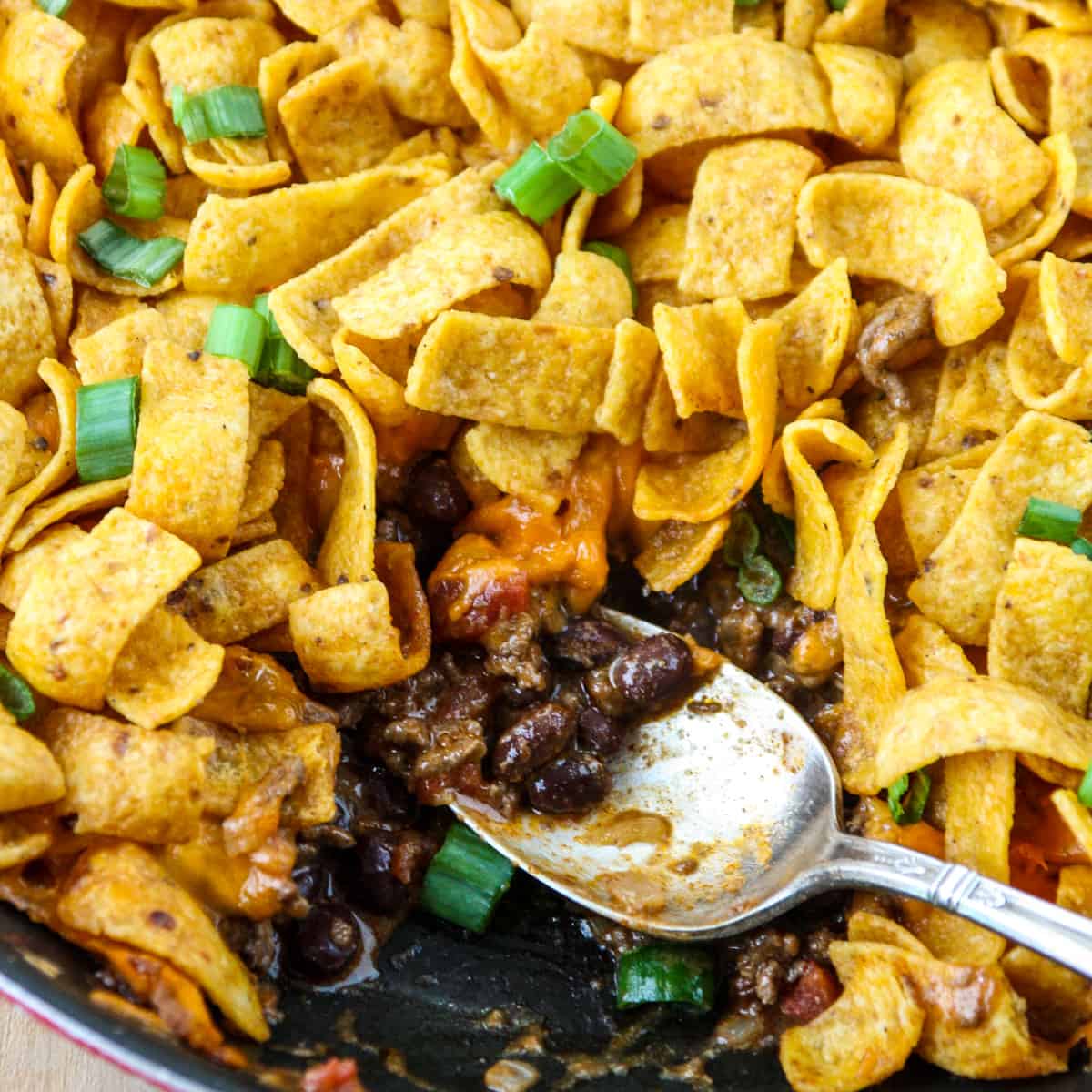 A pan of walking taco casserole with a slice removed and a silver spoon.