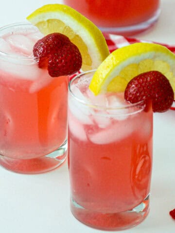 Two glasses of rhubarb lemonade, garnished with lemon slices and strawberries.