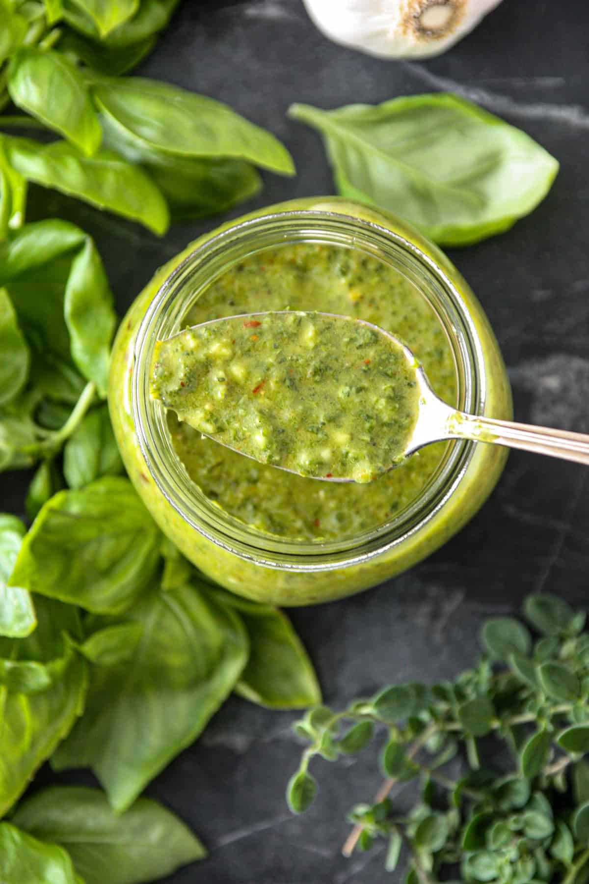 A spoonful of basil chimichurri sauce on top of a glass jar with sauce.
