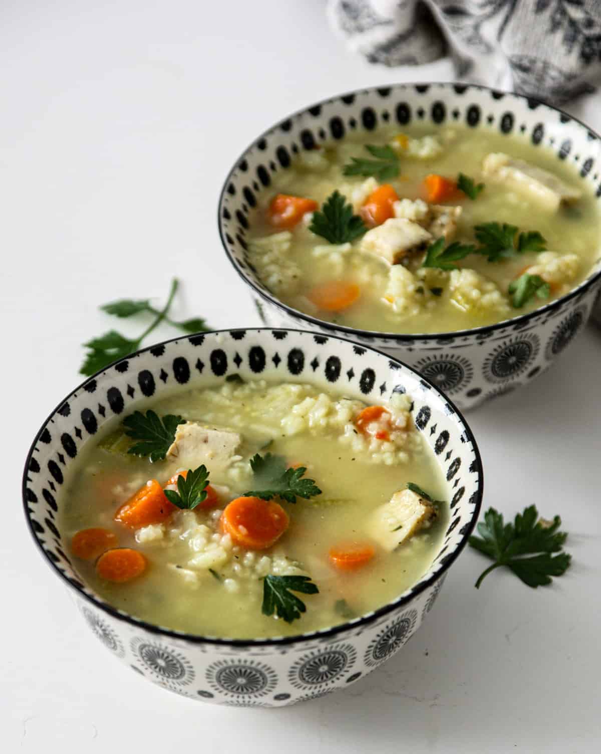 Two bowls of turkey and rice soup on a white countertop. 