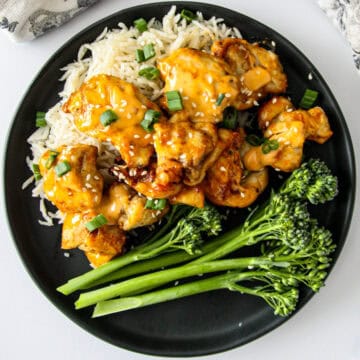 Bang bang chicken is on top of rice on a black plate.