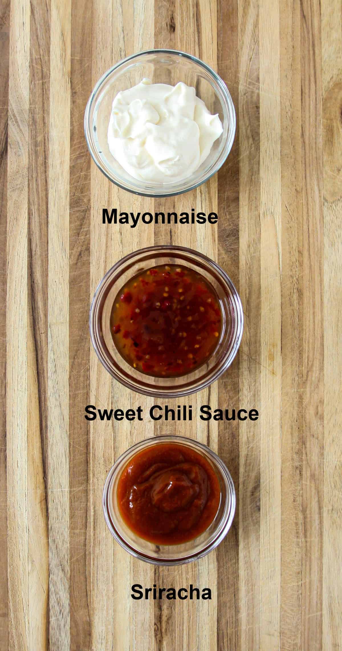 Ingredients for making bang bang sauce in a glass bowl on a wooden board.