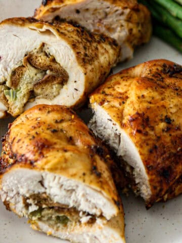 Four stuffed chicken breast halves on a white plate.