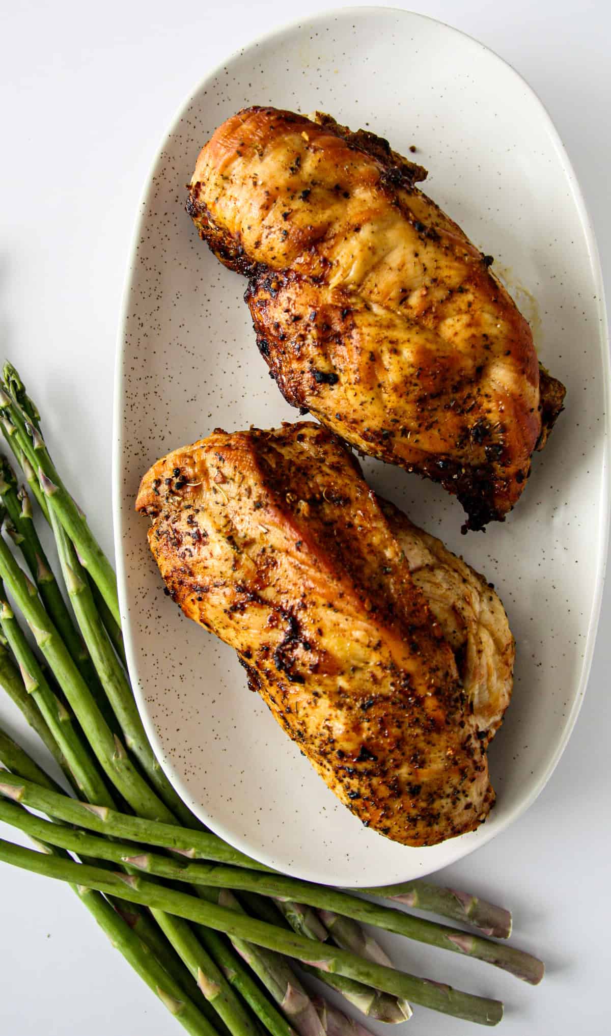 Two baked, stuffed chicken breasts with stuffing on a white speckled plate.