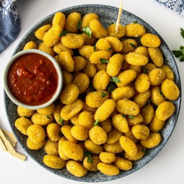 Air fryer gnocchi on a blue plate with a small bowl of marinara dip.