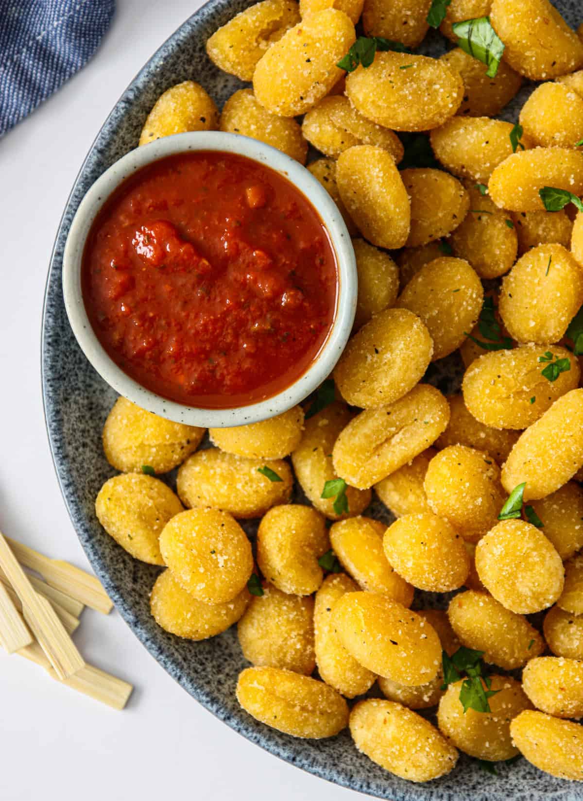 A small plate of air fryer gnocchi and marinara dip is served on a blue-spotted plate.
