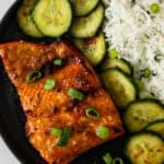 A fillet of miso butter salmon on a black plate.