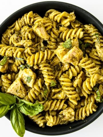 Tuna pesto pasta in a black bowl with a sprig of basil.