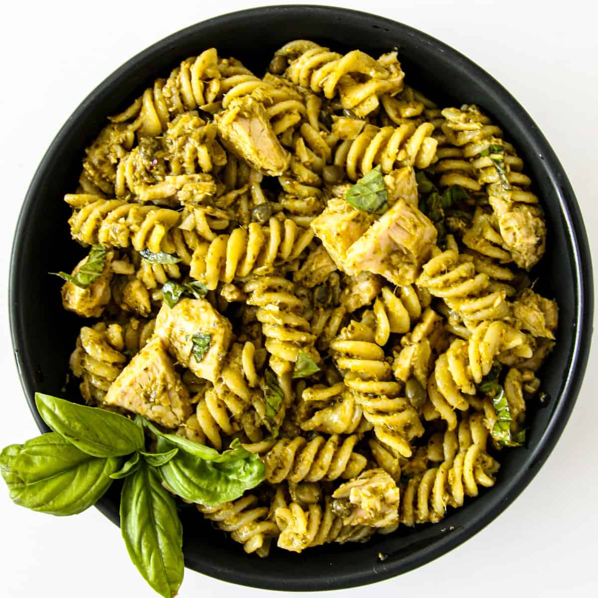 Tuna pesto pasta in a black bowl with a sprig of basil.