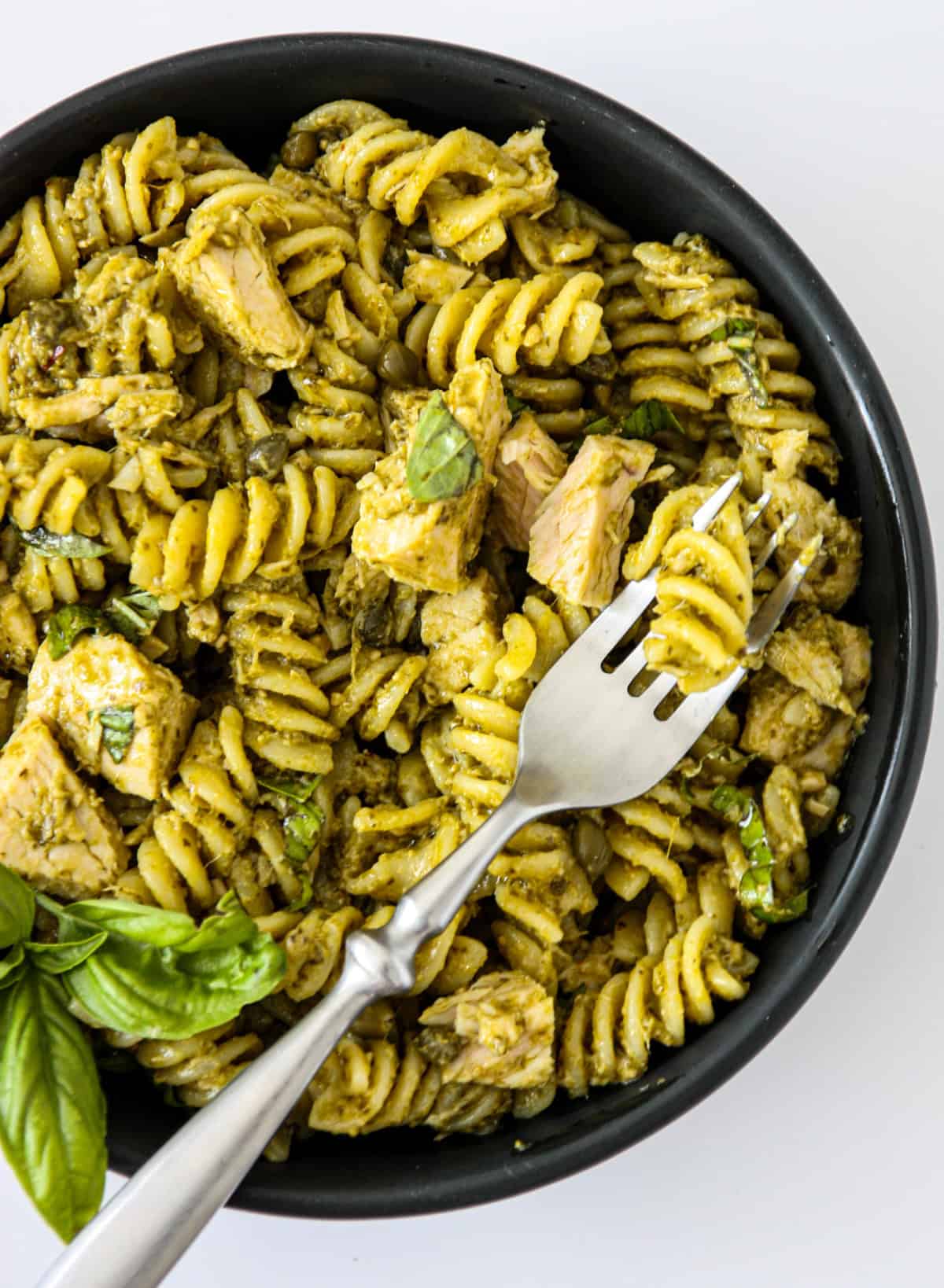 Tuna pesto pasta in a black bowl with a fork inserted.