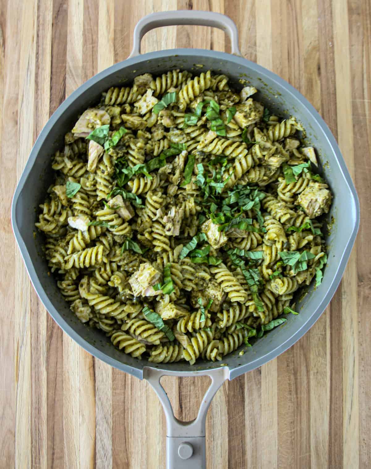 Tuna pesto pasta in a skillet, garnished with chopped basil.
